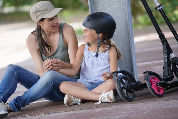 Young girl with mom sitting on floor after riding scooters - Zdjęcie, obraz