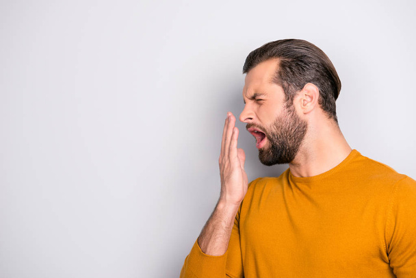 Side profile half-faced portrait of tired sleepy bored handsome bearded unhappy with trendy hairdo guy yawning covering mouth with hand isolated on gray background copy-space - Фото, изображение