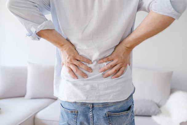 Man is touching his back because it aches. Backache concept bending over in pain with hands holding lower back. Close up of man rubbing his painful back. Pain relief, chiropractic concept - Foto, imagen