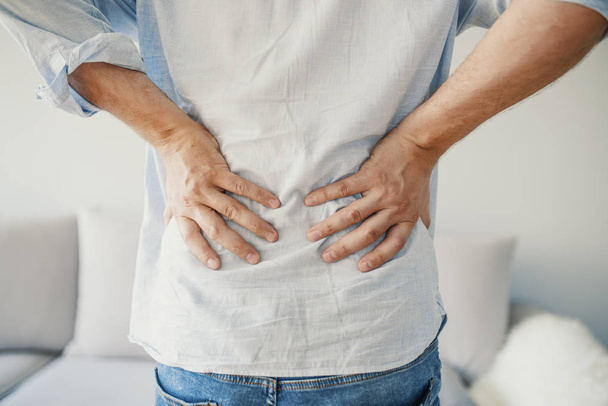 Unhappy man suffering from backache at home. Sport injury, Man with back pain. Acute pain in a male lower back. People, healthcare and problem concept - Φωτογραφία, εικόνα