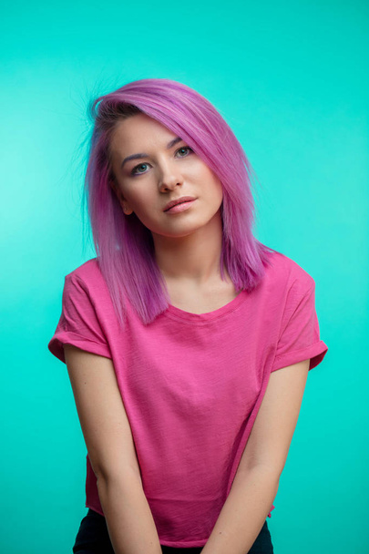 Attractive girl with pink hair, dressed in casual pink cloth on blue background. - Fotó, kép