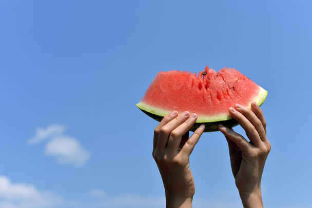 Watermelon in hands against a blue sky with clouds. Piece of watermelon - Foto, Imagem