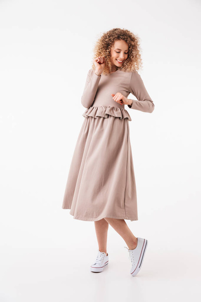 Full length image of Cheerful blonde curly woman in dress posing and looking down over grey background - Foto, Bild