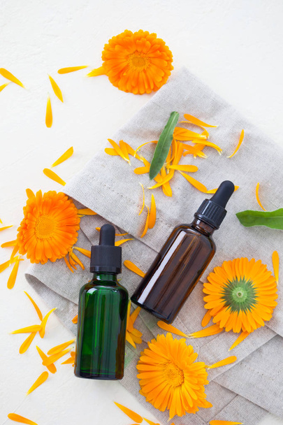 Calendula ätherisches Öl in grünen und braunen Flaschen und frischen Blumen isoliert auf weißem Hintergrund, Schönheitsbehandlungskonzept  - Foto, Bild