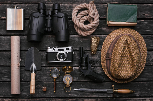 Compass, binoculars, film photo camera, loupe, dagger, handgun, diary book, shovel, rope, gold ore and old scroll document on adventurer or explorer wooden table. Traveler. - Foto, afbeelding