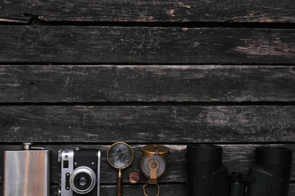Vintage film photo camera, binoculars, magnifying glass, compass and flask on the old table background with copy space. Tourist equipment. - Photo, Image