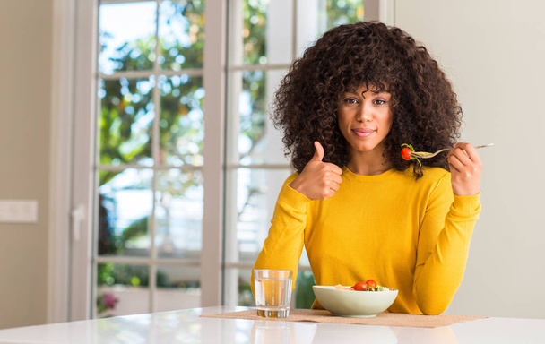 Mujer afroamericana comiendo ensalada de pasta feliz con una gran sonrisa haciendo buen signo, pulgar hacia arriba con los dedos, excelente signo
 - Foto, imagen