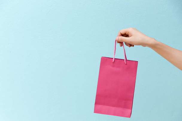 ビジネスの女性の手は青いコンクリート背景にピンクのショッピング バッグを保持します。 - 写真・画像