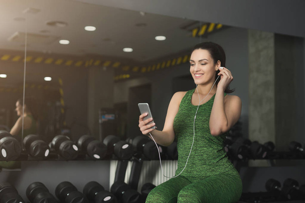 Menina fitness em fones de ouvido escolher música no telefone
 - Foto, Imagem
