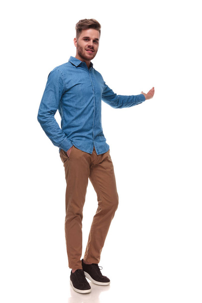 relaxed casual man standing on white background with a hand in pocket and presenting behind - Foto, afbeelding
