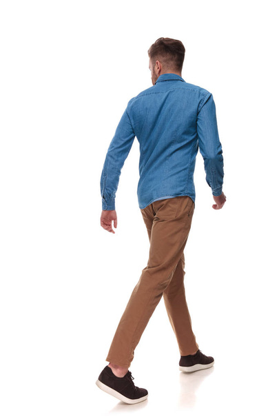 rear view of casual man walking and looking to side on white background, full length picture - 写真・画像