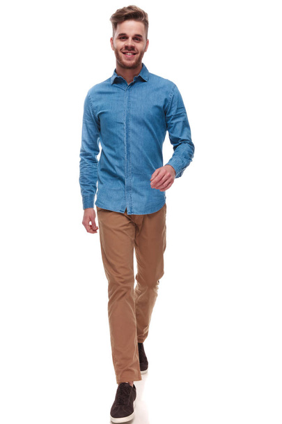 homme décontracté heureux avec chemise bleue marchant vers l'avant sur fond blanc, image pleine longueur
 - Photo, image