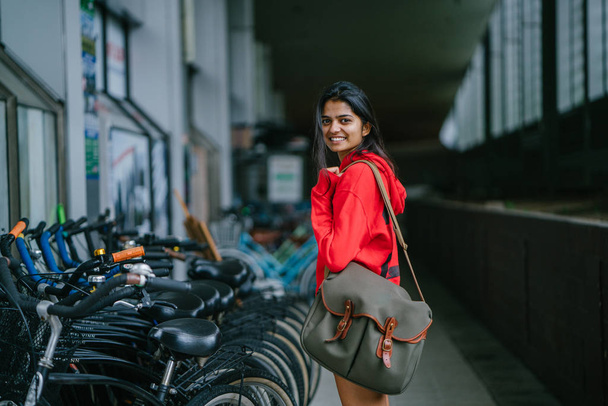 smiling indian girl with bag standing on dark background with parked bikes - Valokuva, kuva