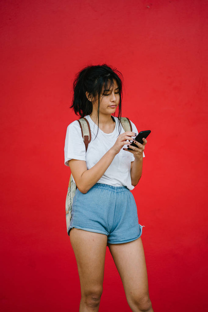 beautiful asian girl smiling holding smartphone standing on studio red background - Fotografie, Obrázek