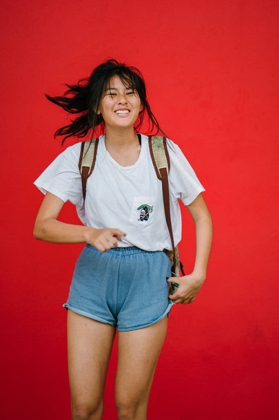 beautiful asian girl with backpack posing on red studio background - Fotoğraf, Görsel
