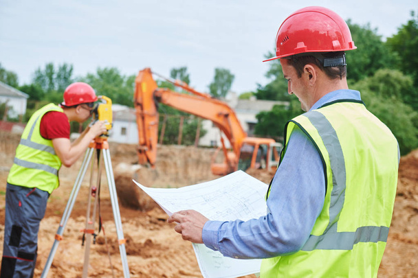 Construction workers on building area. Foreman with blueprint and surveyoor - Foto, imagen