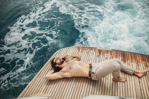 Man relaxing under the sun, lying on a boat at sea. Luxury vacation on a yacht in the islands. - Fotó, kép