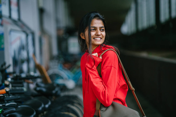 smiling indian girl with bag standing on dark background with parked bikes - Foto, Bild