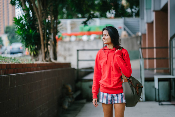 three quarter length portrait of beautiful indian girl wearing casual clothes walking on city street - Фото, зображення