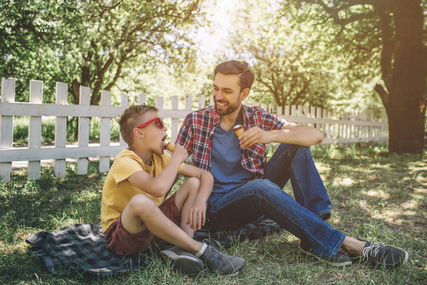 Another cool picture of adult and child sitting together and looking at each other. They are eating ice cream. Small boy wears glasses. - Foto, Imagen