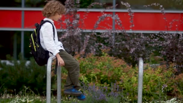 A sad boy sits on the railing in the courtyard near the school. The schoolboy gets up and goes sadly. Psychological problems of adolescence - Video