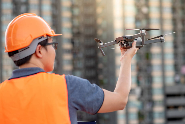 Joven ingeniero asiático sosteniendo dron en el sitio de construcción. Uso de vehículos aéreos no tripulados (UAV) para el estudio de terrenos y obras en proyectos de ingeniería civil
. - Foto, Imagen