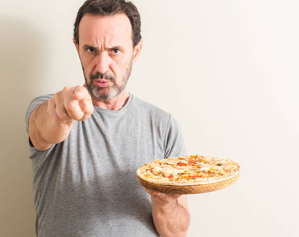 Senior man holding pizza pointing with finger to the camera and to you, hand sign, positive and confident gesture from the front - Photo, Image