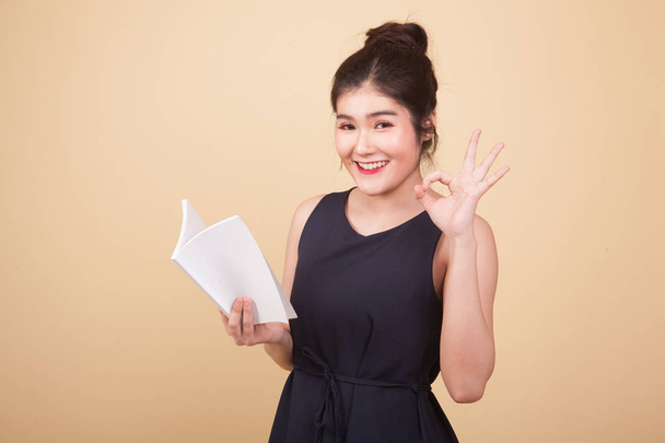 Young Asian woman show OK with a book  on beige background - Zdjęcie, obraz