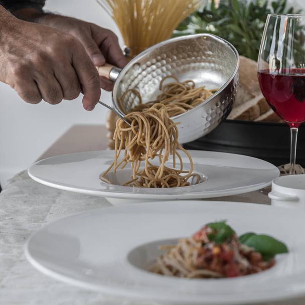 Closeup of male cook serving spaghetti topped with delicious bolognaise sauce and basil - Fotoğraf, Görsel