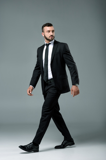 handsome businessman in suit walking and looking away on grey - Fotoğraf, Görsel