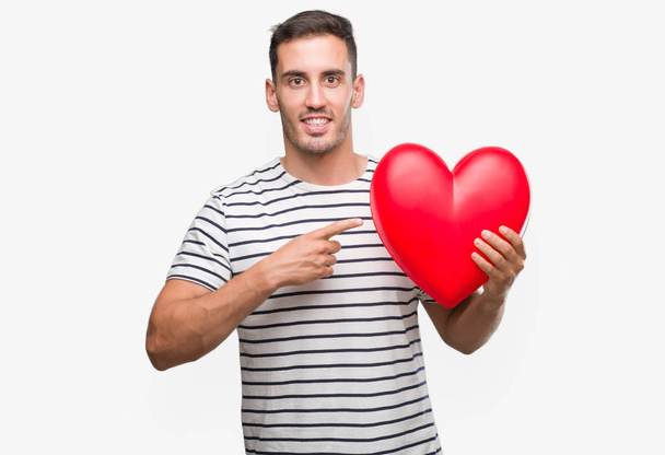 Kırmızı kalp çok mutlu el ve parmak ile işaret tutan aşık yakışıklı genç adam - Fotoğraf, Görsel