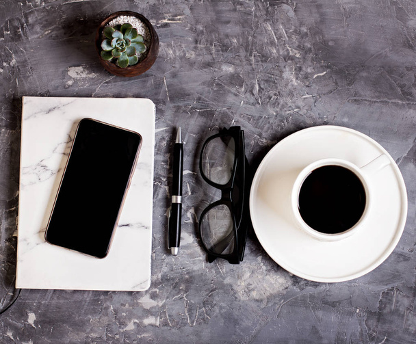 Το σημειωματάριο, κινητό τηλέφωνο, στυλό, χυμώδεις, γυαλιά, φλιτζάνι καφέ σε φόντο γκρι τσιμέντο. Επιχειρηματική ιδέα. - Φωτογραφία, εικόνα
