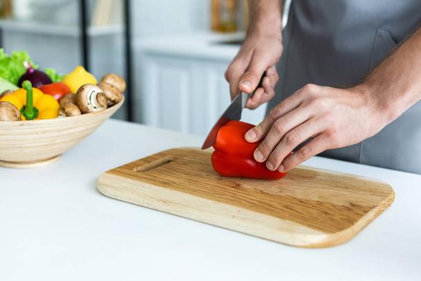 cropped shot of man in apron cutting bell pepper on wooden cutting board  - Photo, Image