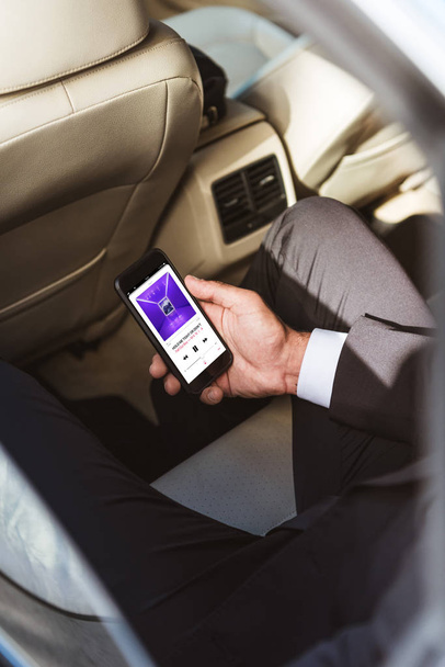 cropped image of businessman holding smartphone and listening to fall out boy band in car - 写真・画像
