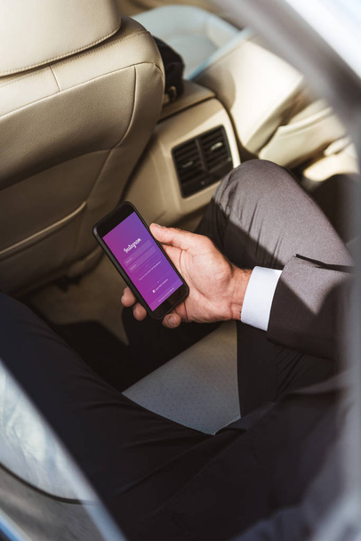 cropped image of businessman holding smartphone with loaded instagram page in car - Photo, Image