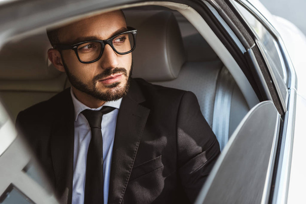 handsome businessman sitting in car and looking away - Zdjęcie, obraz