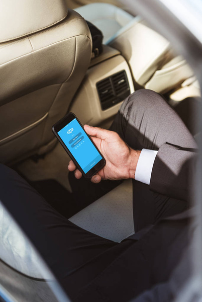 cropped image of businessman holding smartphone with loaded skype page in car - Fotografie, Obrázek