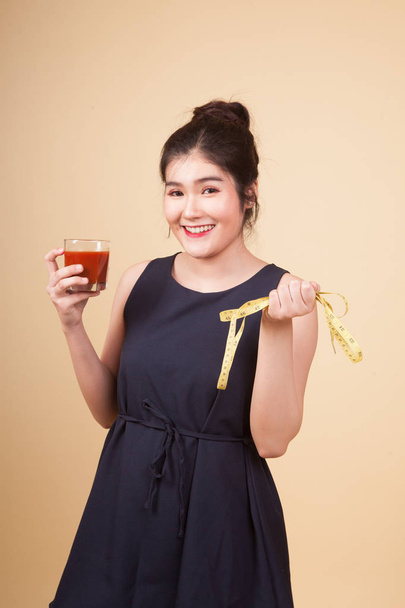 Young healthy Asian woman with dumbbell and  tomato juice  on beige background - Photo, image