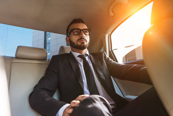 handsome businessman in suit sitting in car during sunset - Foto, Imagen