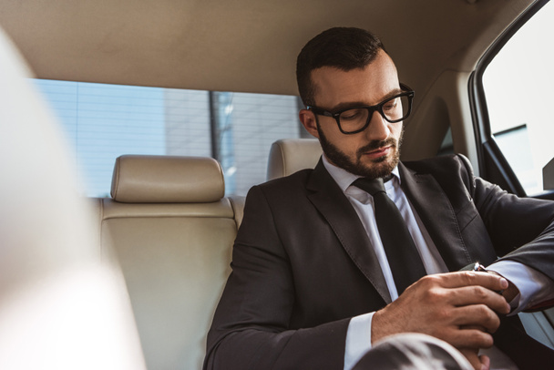 handsome businessman checking time on wristwatch in car - 写真・画像