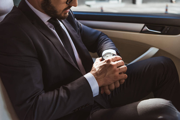 cropped image of businessman in suit checking time on wristwatch in car - Fotoğraf, Görsel