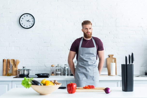 handsome bearded young man in apron cooking in kitchen - Valokuva, kuva
