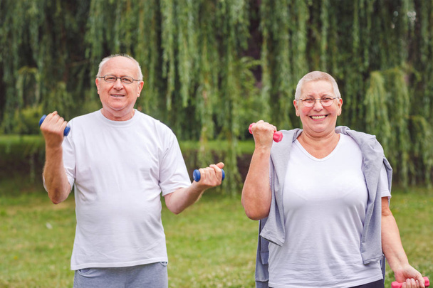 senior homme et femme pratiquent exercice de fitness avec haltères dans un parc à la journée ensoleillée
 - Photo, image