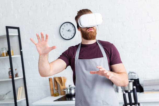 young man in apron using virtual reality headset in kitchen   - Foto, Bild
