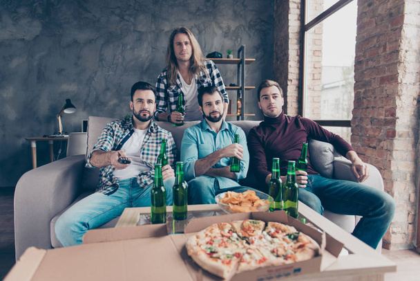 Four attractive stylish bearded guys with modern hairstyle in denim outfit sitting together in living room using remote controller, trying to find program, comedy, sport channel on television - Photo, Image