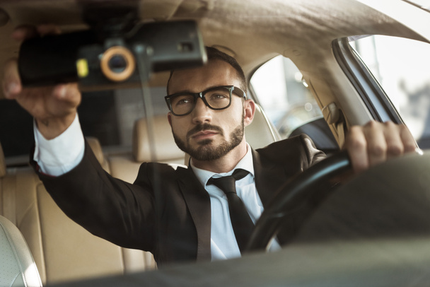 красивый водитель в костюме водителя автомобиля и ремонт зеркала
 - Фото, изображение