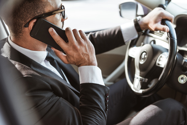 vista lateral del conductor guapo en traje coche de conducción y hablar por teléfono inteligente
 - Foto, Imagen