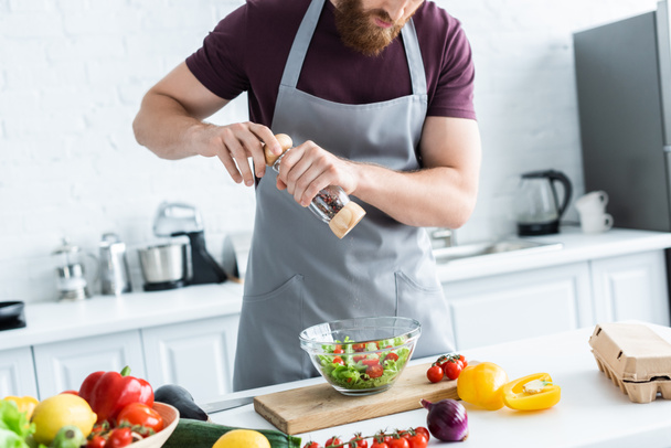 cropped shot of bearded man in apron cooking vegetable salad - Valokuva, kuva