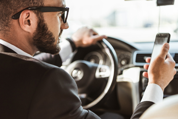 handsome driver in suit driving car and holding smartphone - Foto, Bild