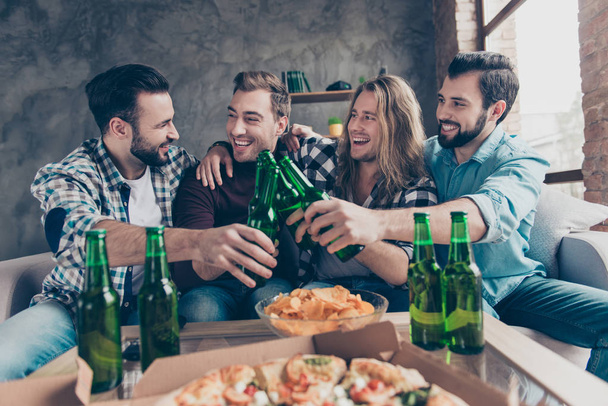 Stylish, bearded, successful guy said funny toast, his stylish friends with modern hairstyle looking at him and laughing, team of four persons clinking bottles with lager, having snacks on the table - Photo, image